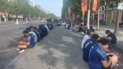 坐成一排,迟到的巴黎球迷用手机在香榭丽舍大道观赛